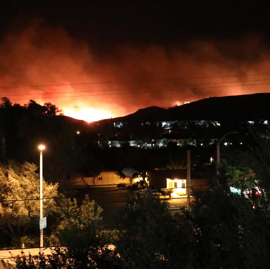 Fire behind hills at night, street lights in foreground